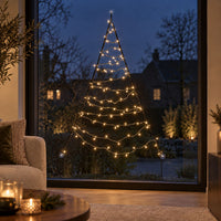 Warm white lights of the Fairybell Premium Window Tree 1.25 metre against the glass with candles and a sofa in the foreground