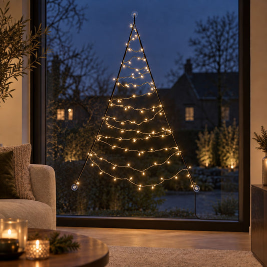 Warm white lights of the Fairybell Premium Window Tree 1.25 metre against the glass with candles and a sofa in the foreground
